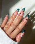 Hand with emerald green French tip press-on nails featuring star and jewel accents