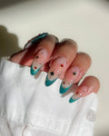 Hand with almond-shaped emerald green French tip press-on nails featuring gold star and jewel accents