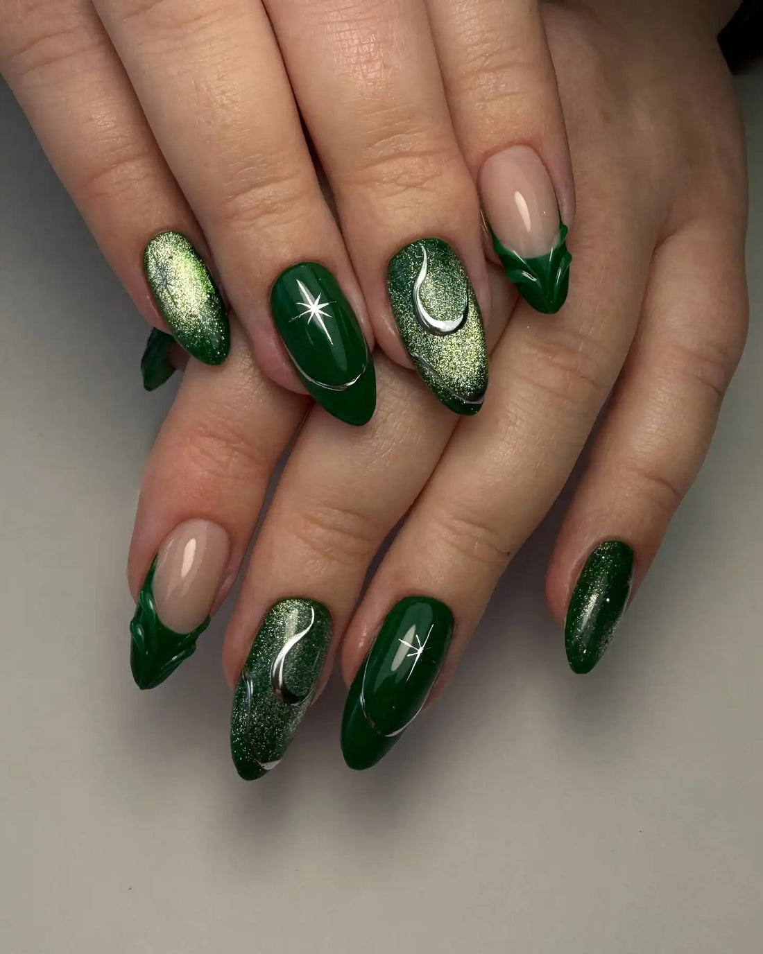 Hand with emerald green press-on nails featuring celestial moon and star designs