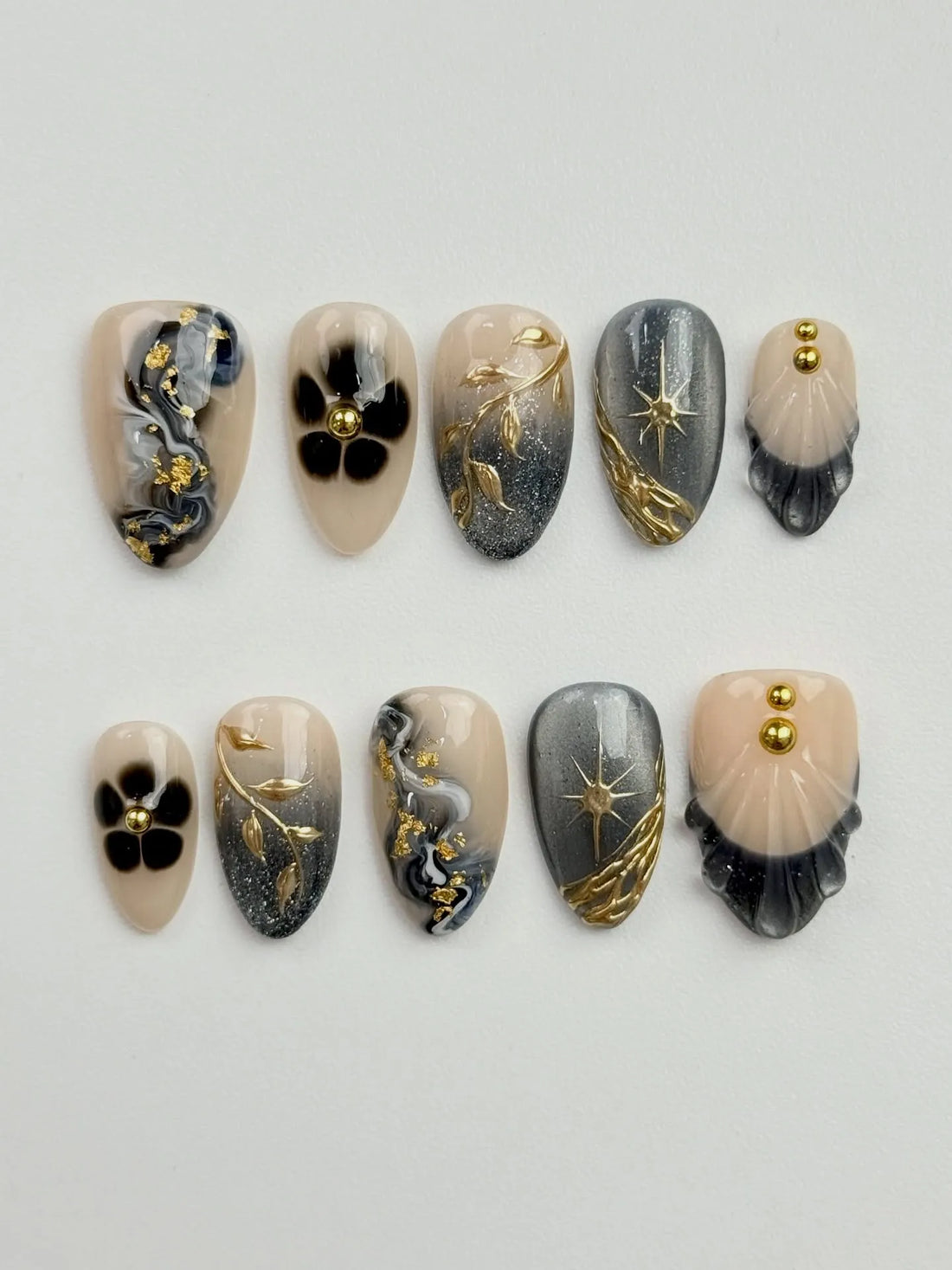 Handmade press-on nails with grey marble, gold celestial starburst, floral, and shell designs.