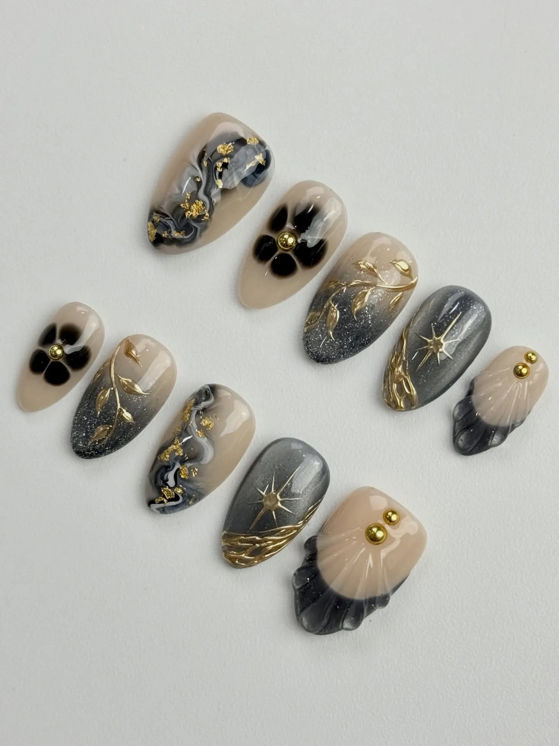 Handmade press-on nails with grey marble, gold celestial starburst, floral, and shell designs.