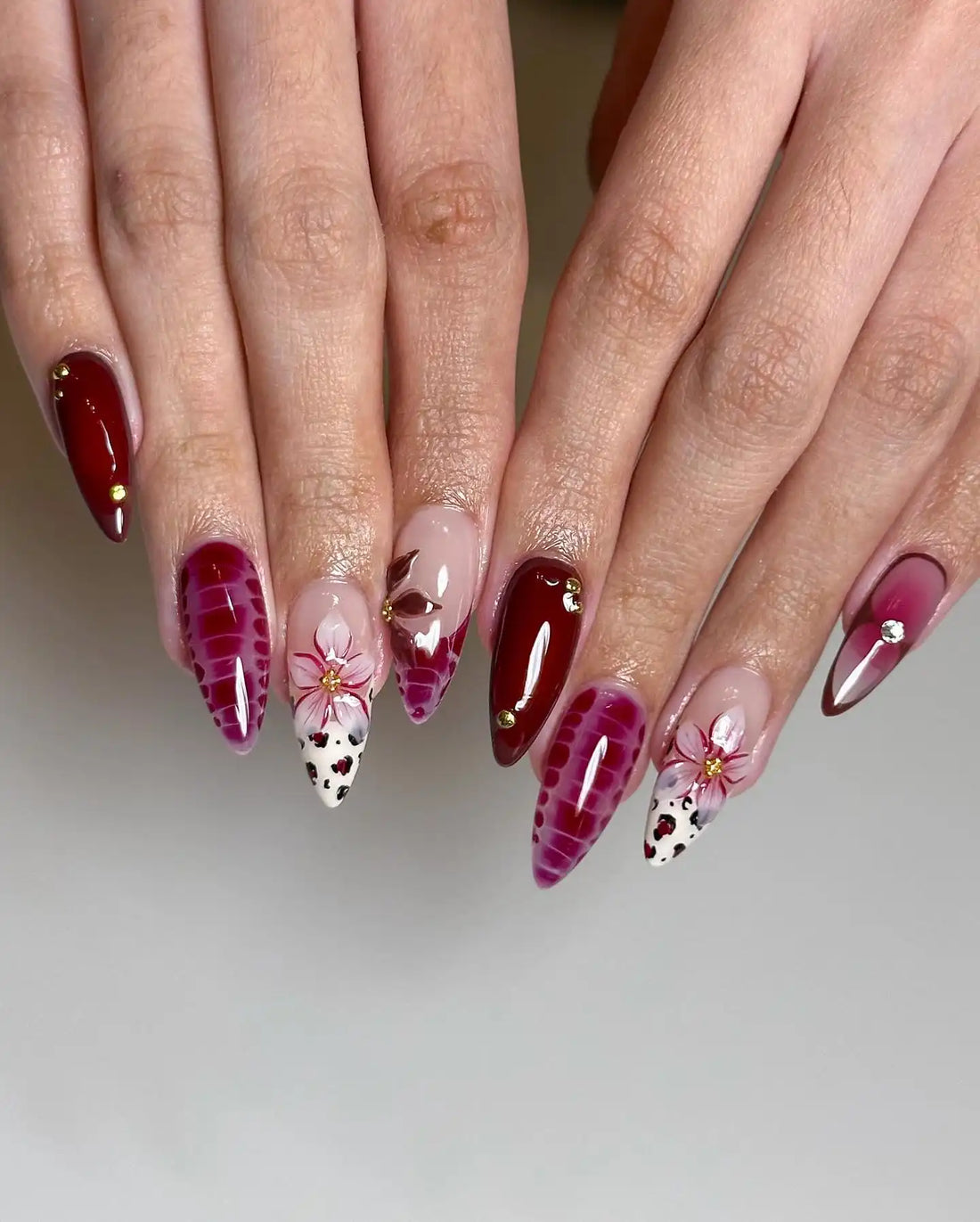 Handmade red press-on nails with floral designs, gold accents, and spring-inspired patterns.