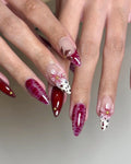 Hand with handmade press-on nails featuring red floral designs, spring patterns, and gold accents.