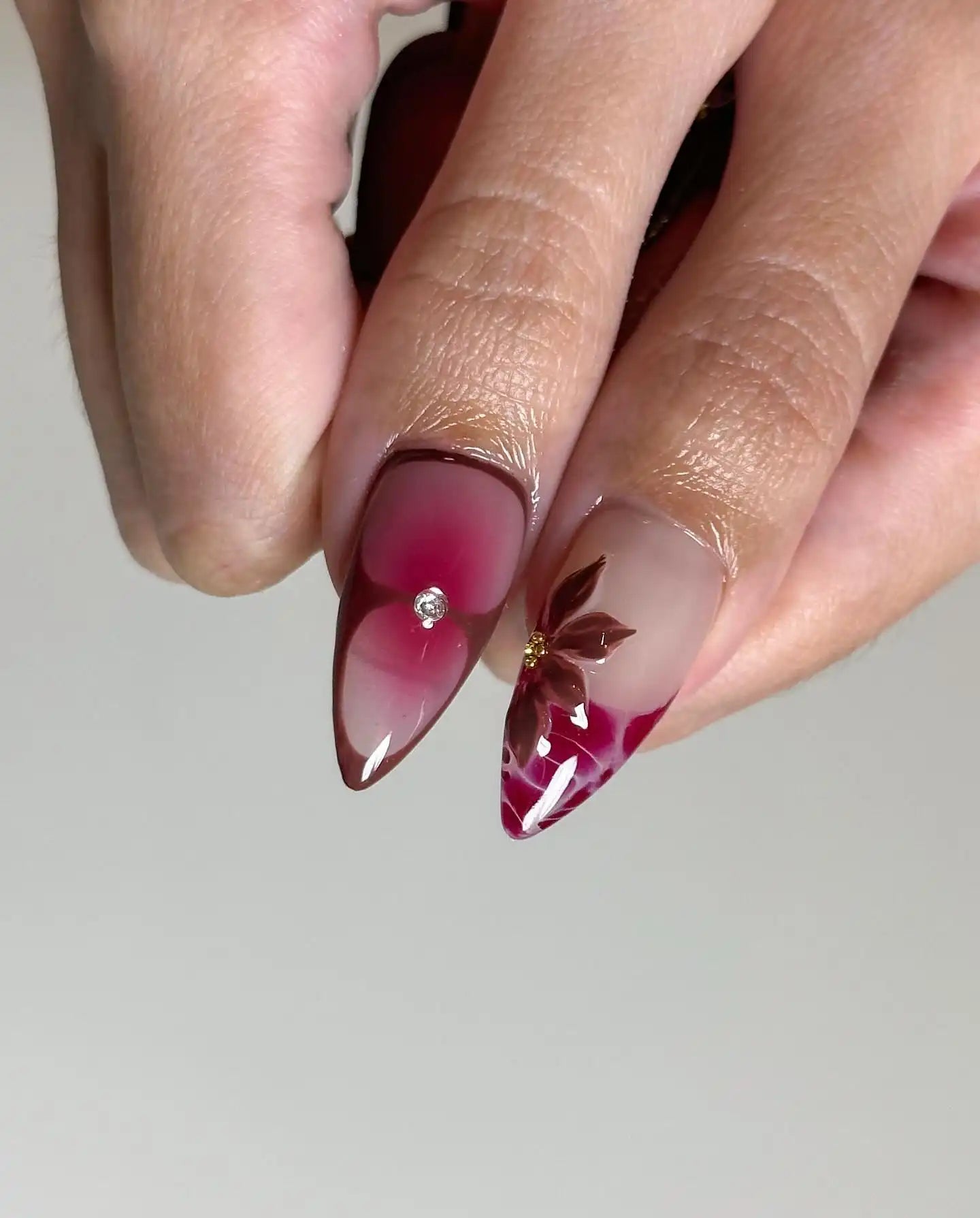 Hand with handmade red floral spring press-on nails featuring rhinestone accents.