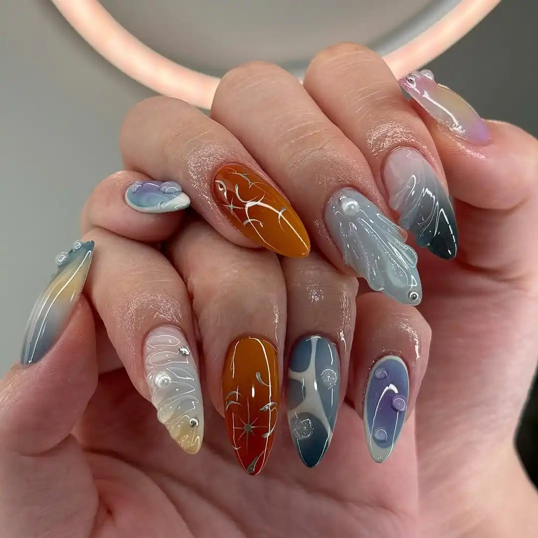 Hand holding long handmade ombre press-on nails with colorful aura designs and 3D accents