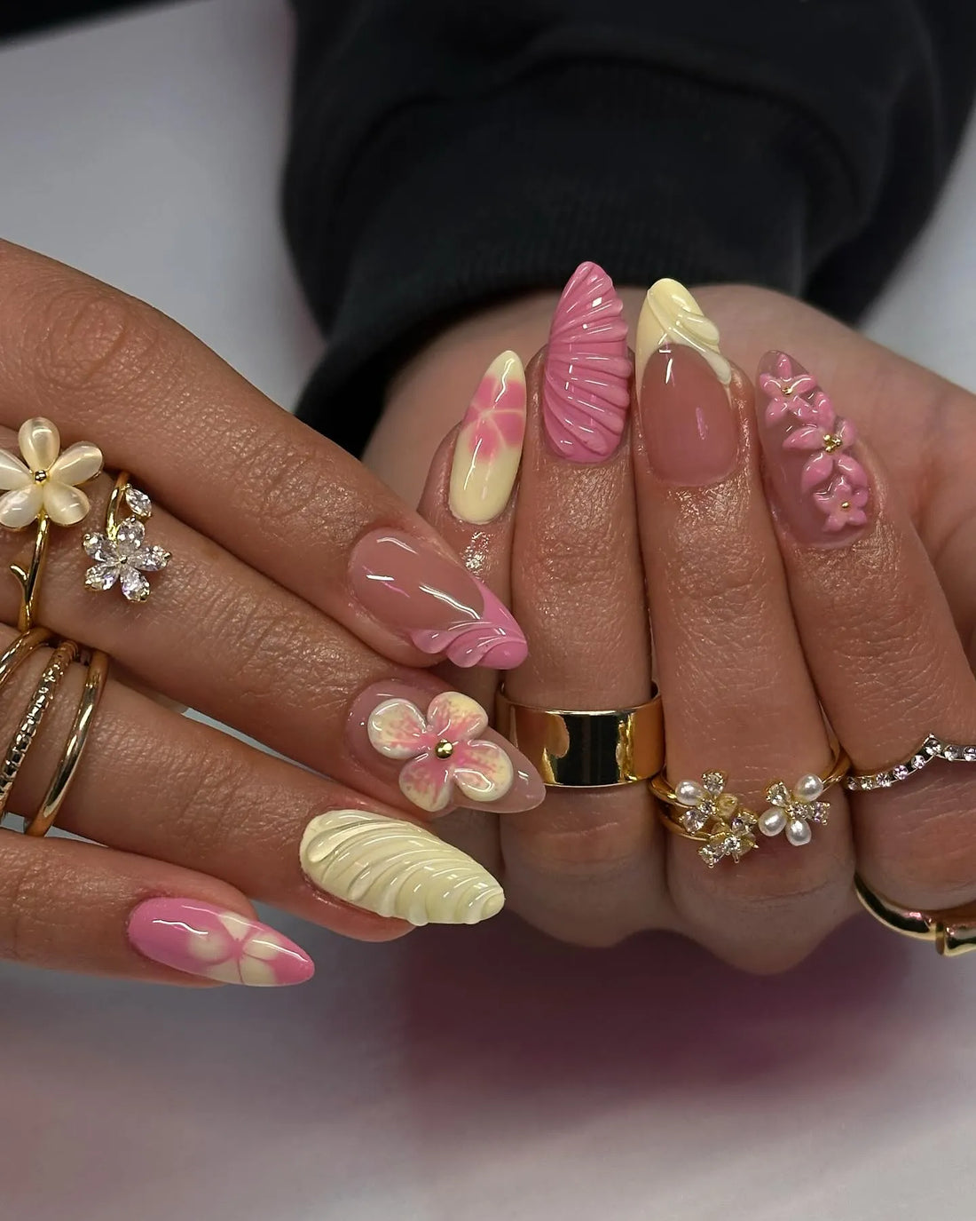 Hand with long pink and yellow press-on nails, 3D flower and shell designs, spring nail art
