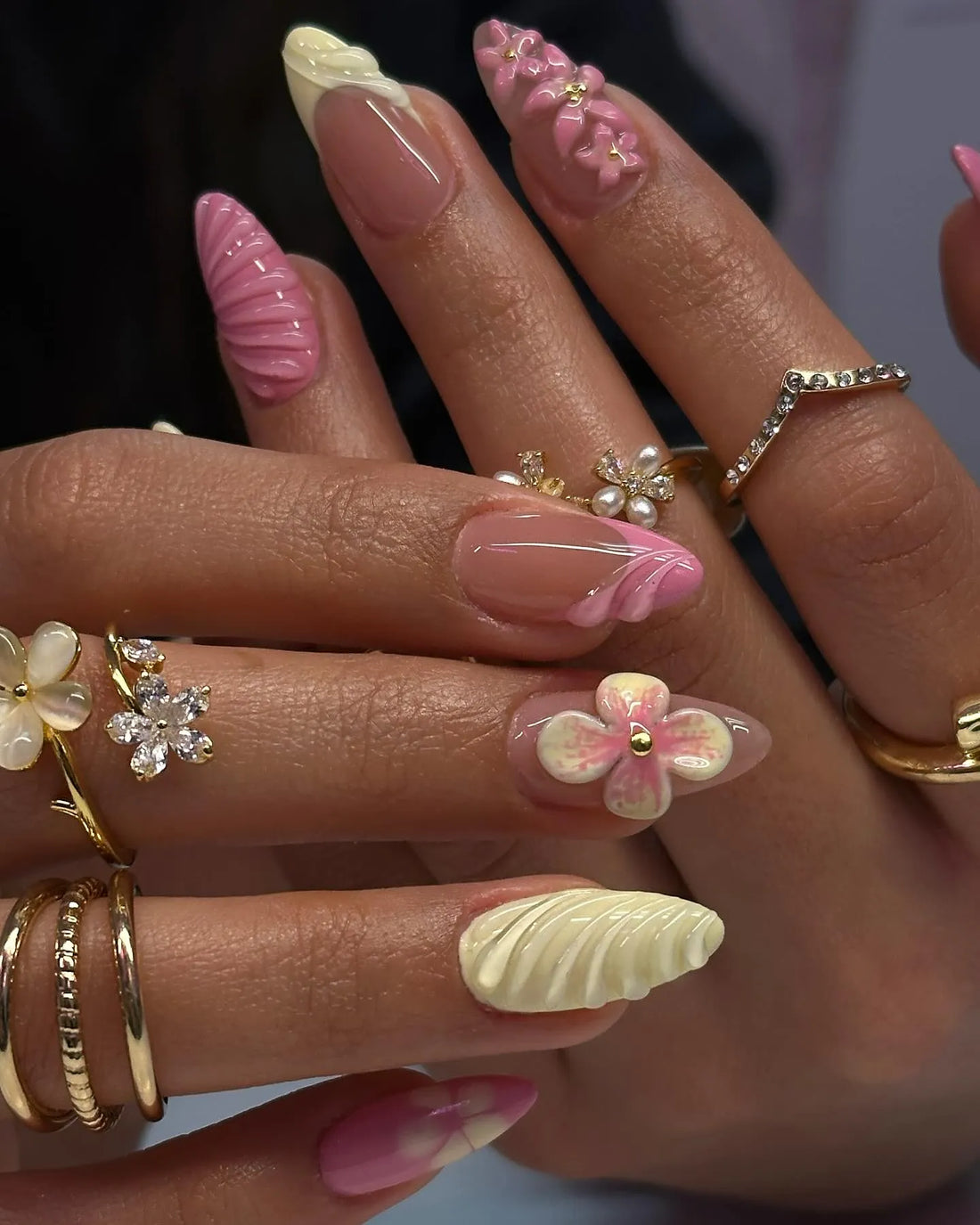Hand with long pink and yellow press-on nails, 3D flower and shell designs, spring nail art