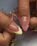 Hand holding sculpted press-on nails with glossy pink and yellow 3D floral tips.