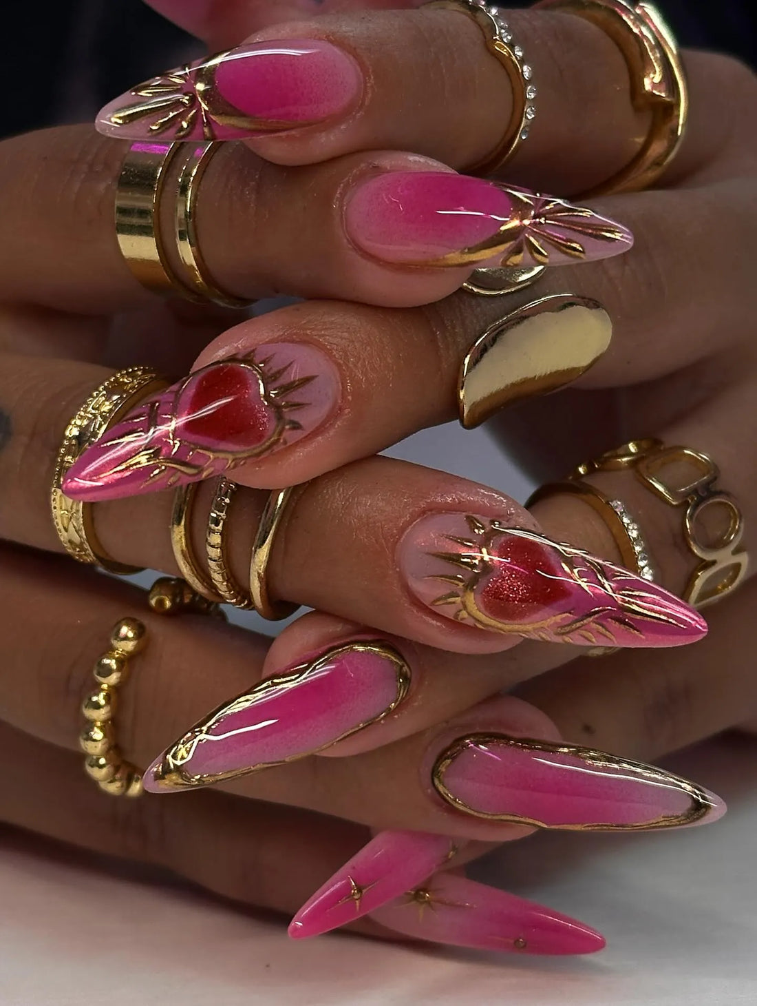 Hand with long hot pink ombre press-on nails, gold chrome accents, and sacred heart designs.