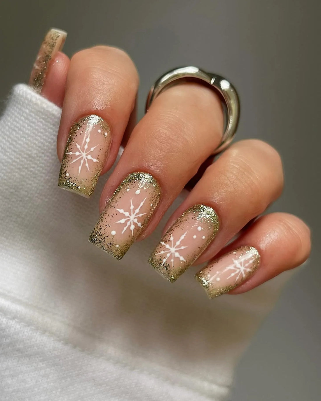 Hand showing gold glitter ombre press-on nails with white snowflake holiday nail art.