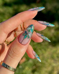 Hand holding green floral stained glass press-on nails with elegant art design outdoors