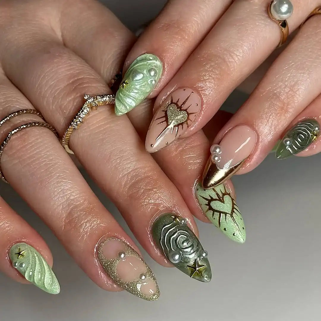 Hand with green and gold celestial press-on nails, heart, pearl, and star textured designs