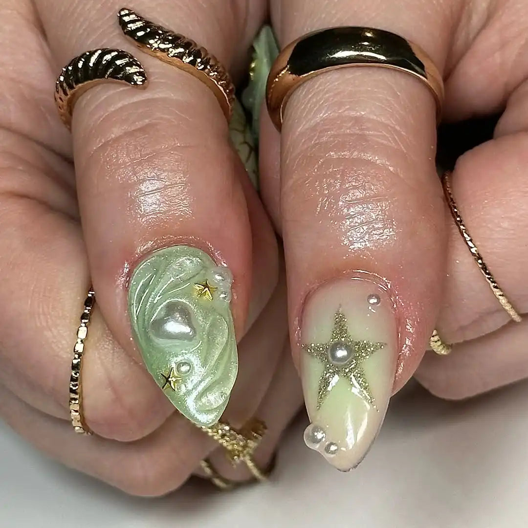 Hand with green and gold celestial press-on nails, heart, pearl, and star textured designs