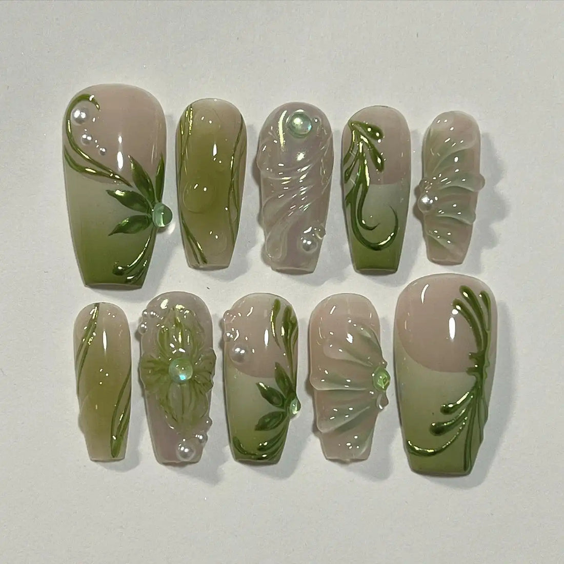 Handmade green leaf and floral press-on nails with 3D details on a neutral background