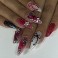 Hand with long stiletto press-on nails in black, red, and chrome, featuring bows, stars, crosses, and 3D accents.