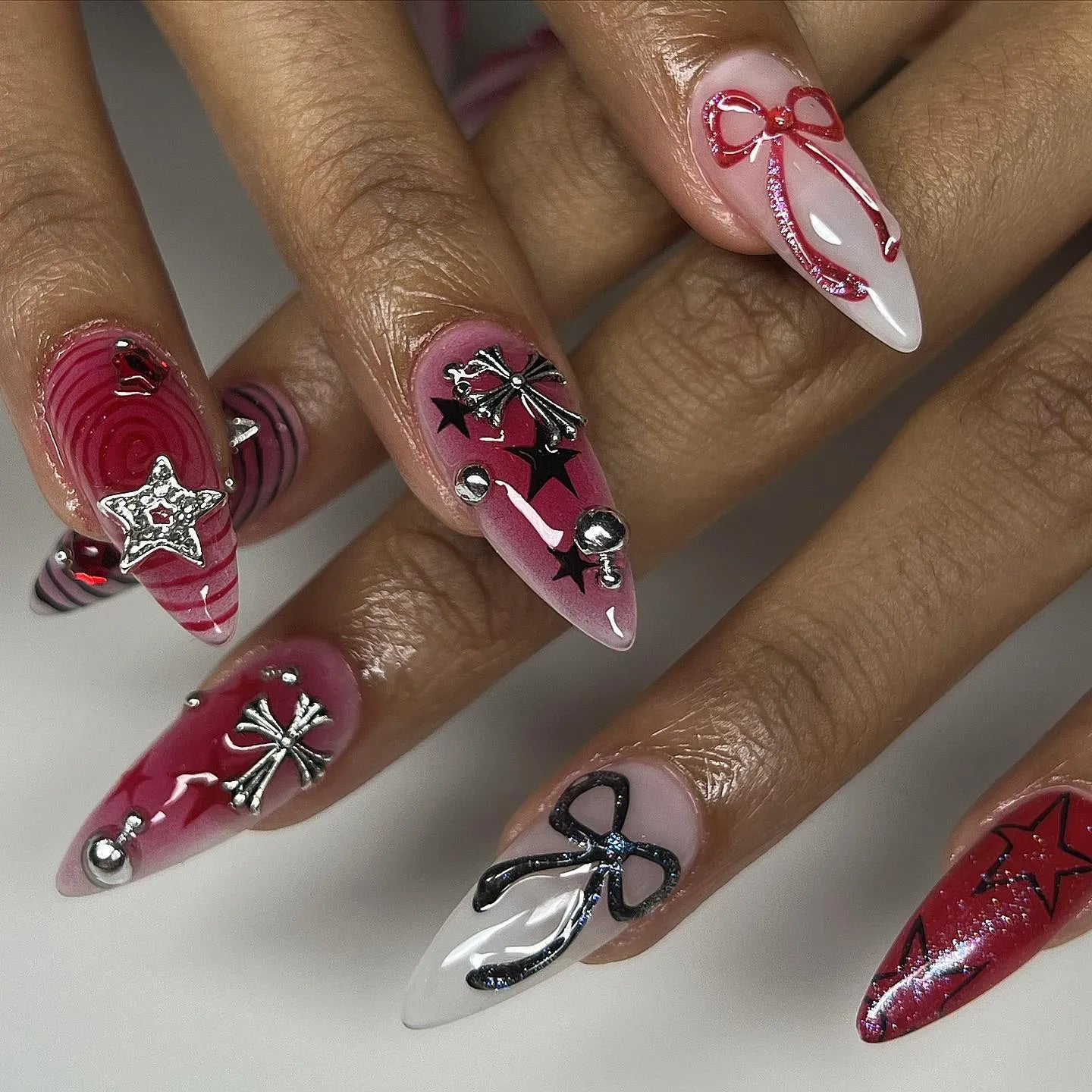 Handmade grunge goth red and black press-on nails with chrome cross, star, and ribbon designs.