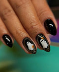 Hand with black press-on nails, two nails feature cute ghost and metallic Halloween accents.
