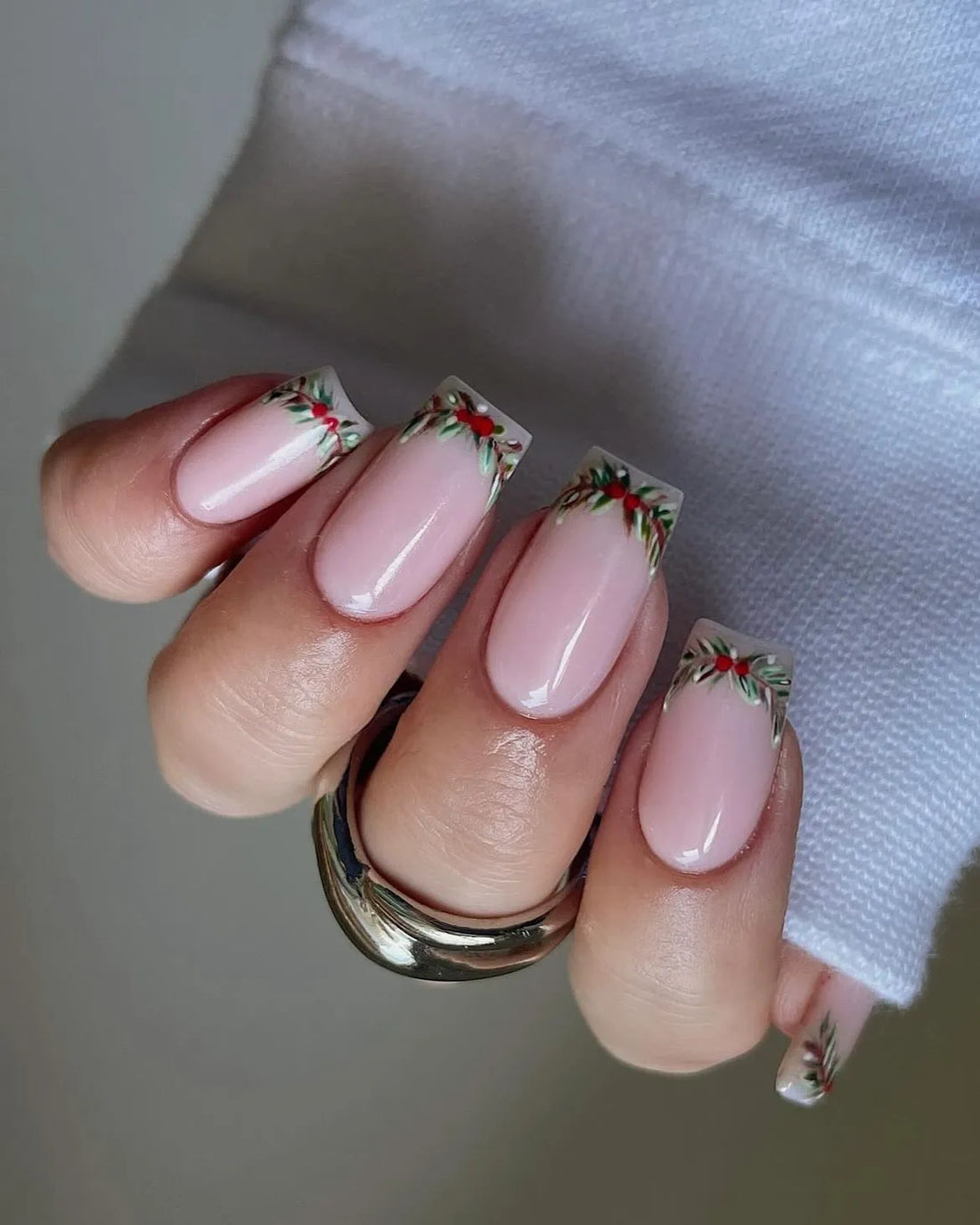 Hand with nude French tip press-on nails featuring holly berry festive Christmas design