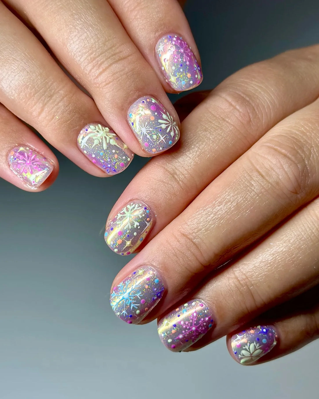 Hand with handmade pastel snowflake press-on nails featuring holo confetti glitter.