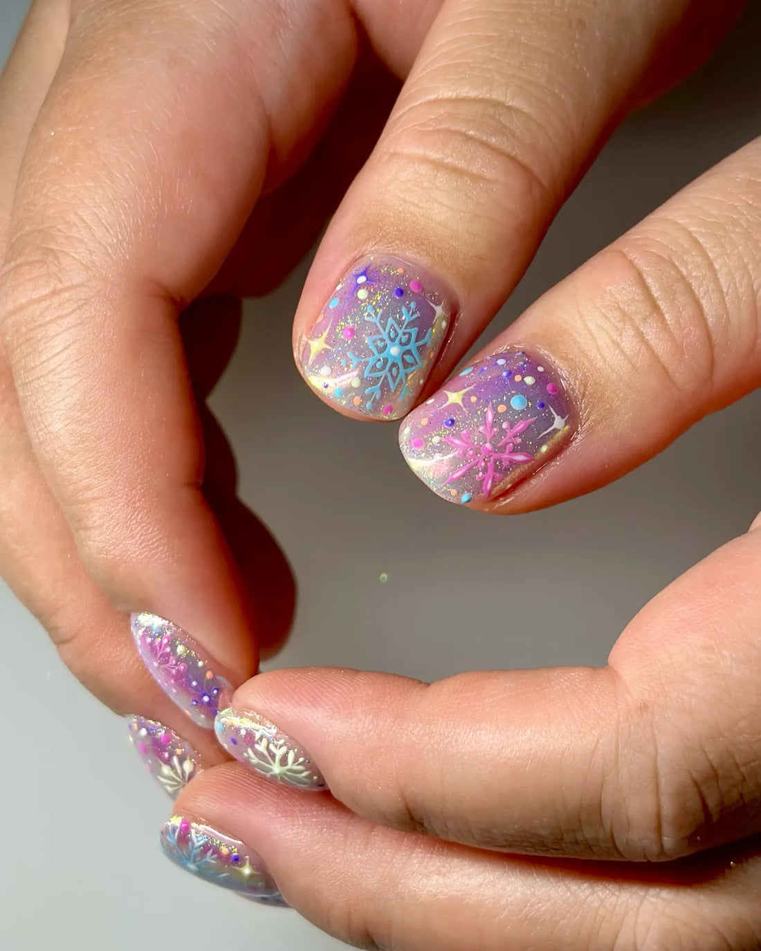 Hand with handmade pastel snowflake press-on nails featuring holo confetti glitter.