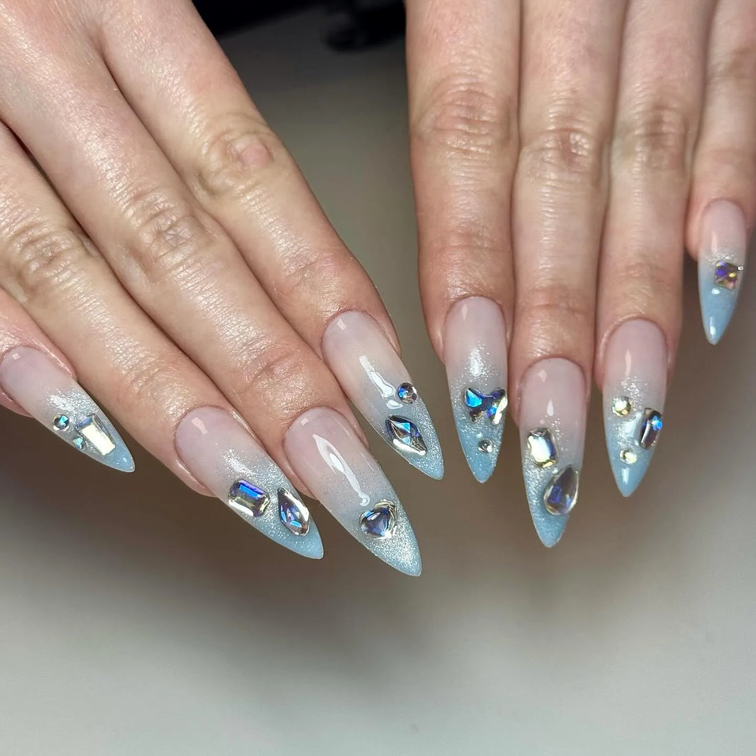 Handmade icy light blue ombre press-on nails with shimmer and gemstone accents.