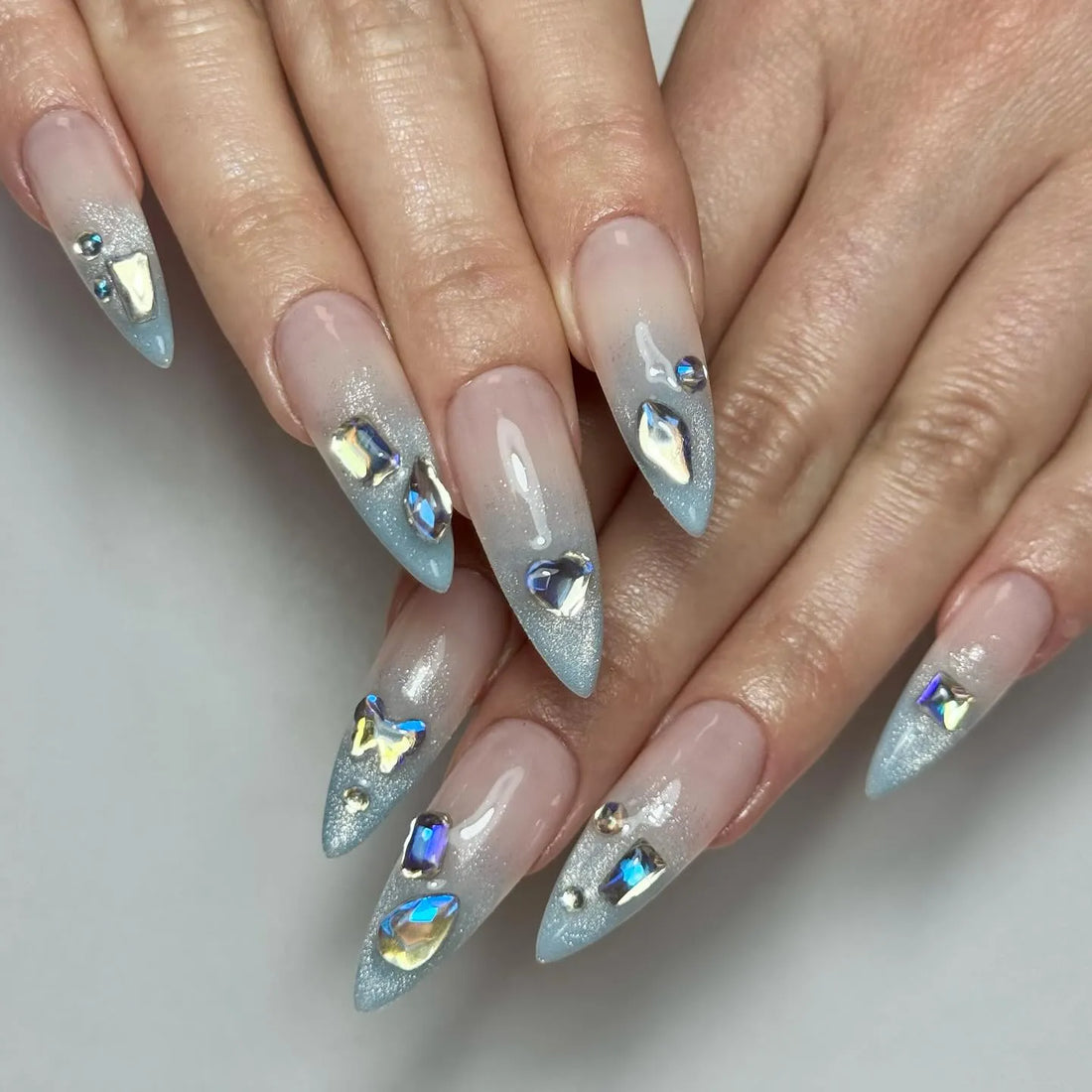 Handmade icy light blue ombre press-on nails with shimmer and gemstone accents.