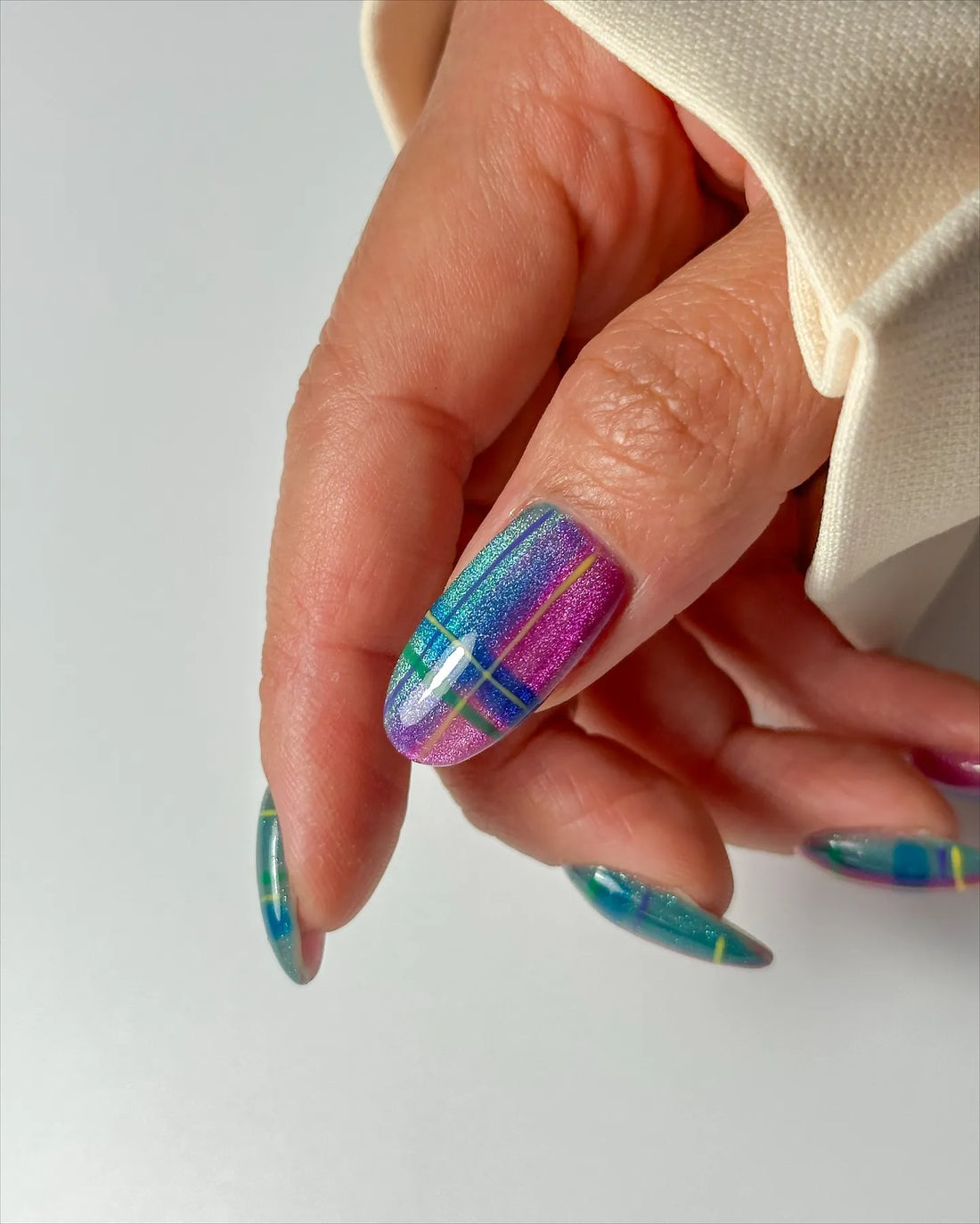 Hand with handmade iridescent neon plaid cat-eye shimmer press-on nails in blue and purple.