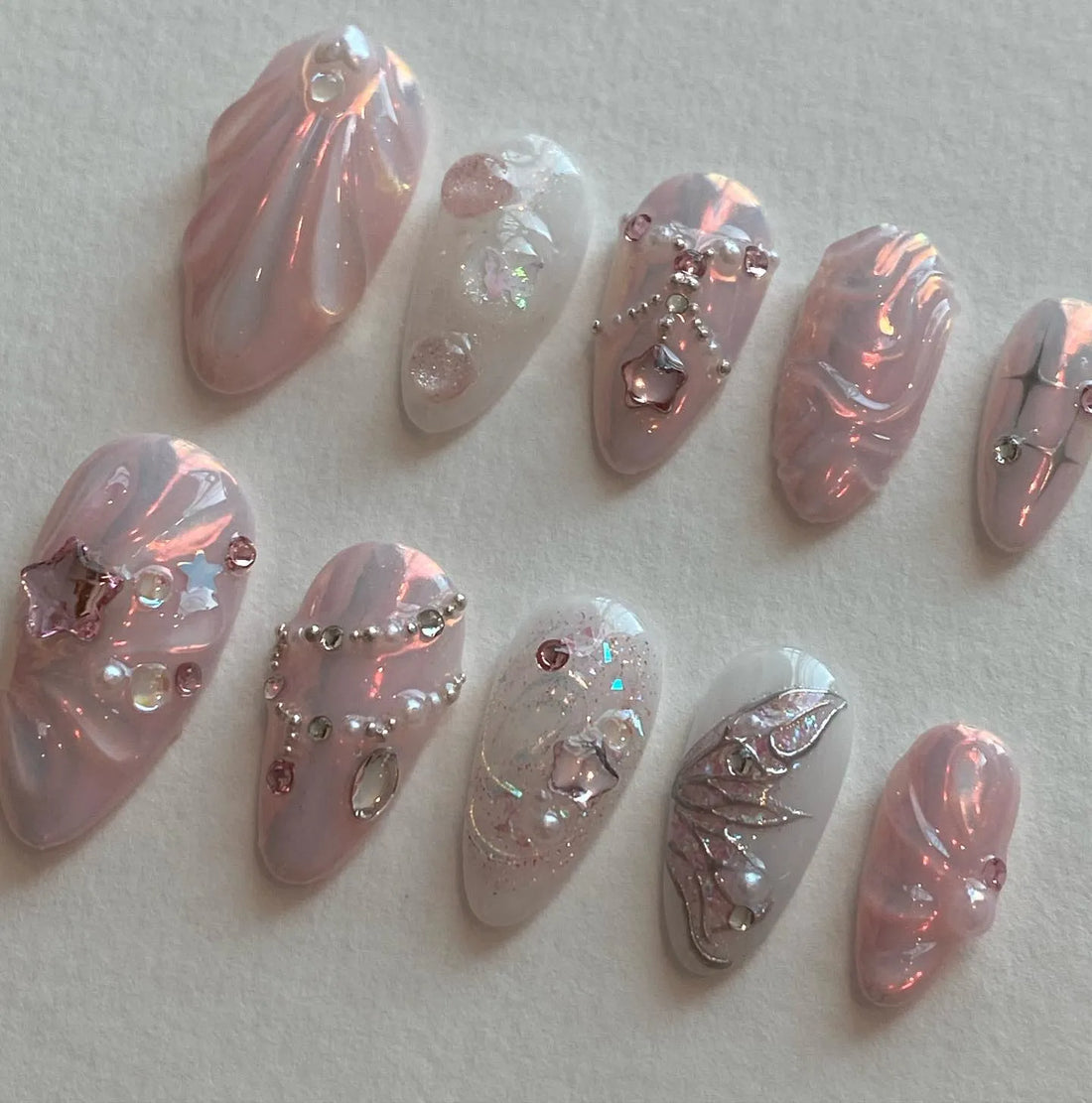 Handmade iridescent pearl pink press-on nails with butterfly, rhinestone, and star accents