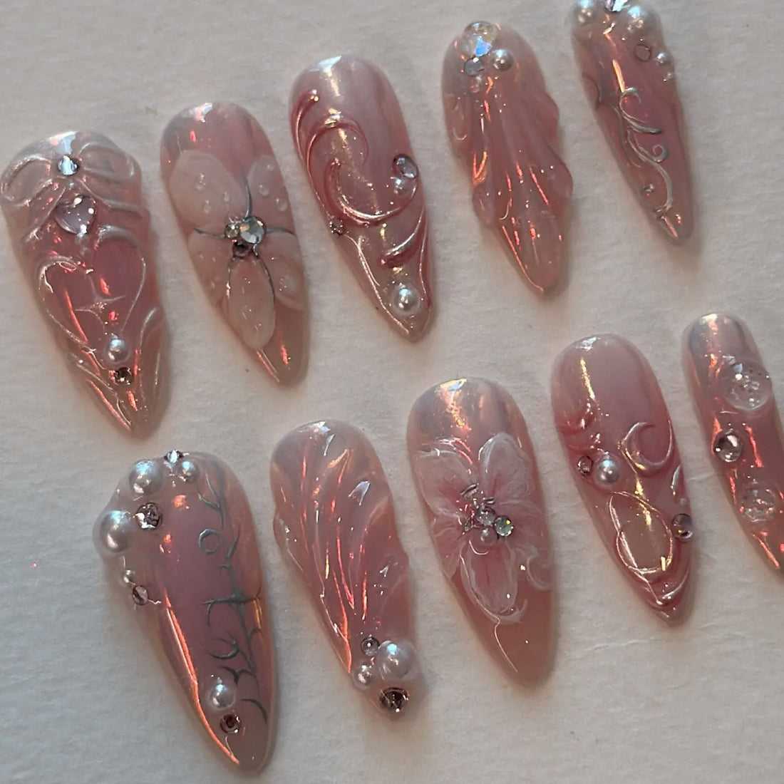 Handmade iridescent pink press-on nails with pearl, rhinestone, floral, and vine designs