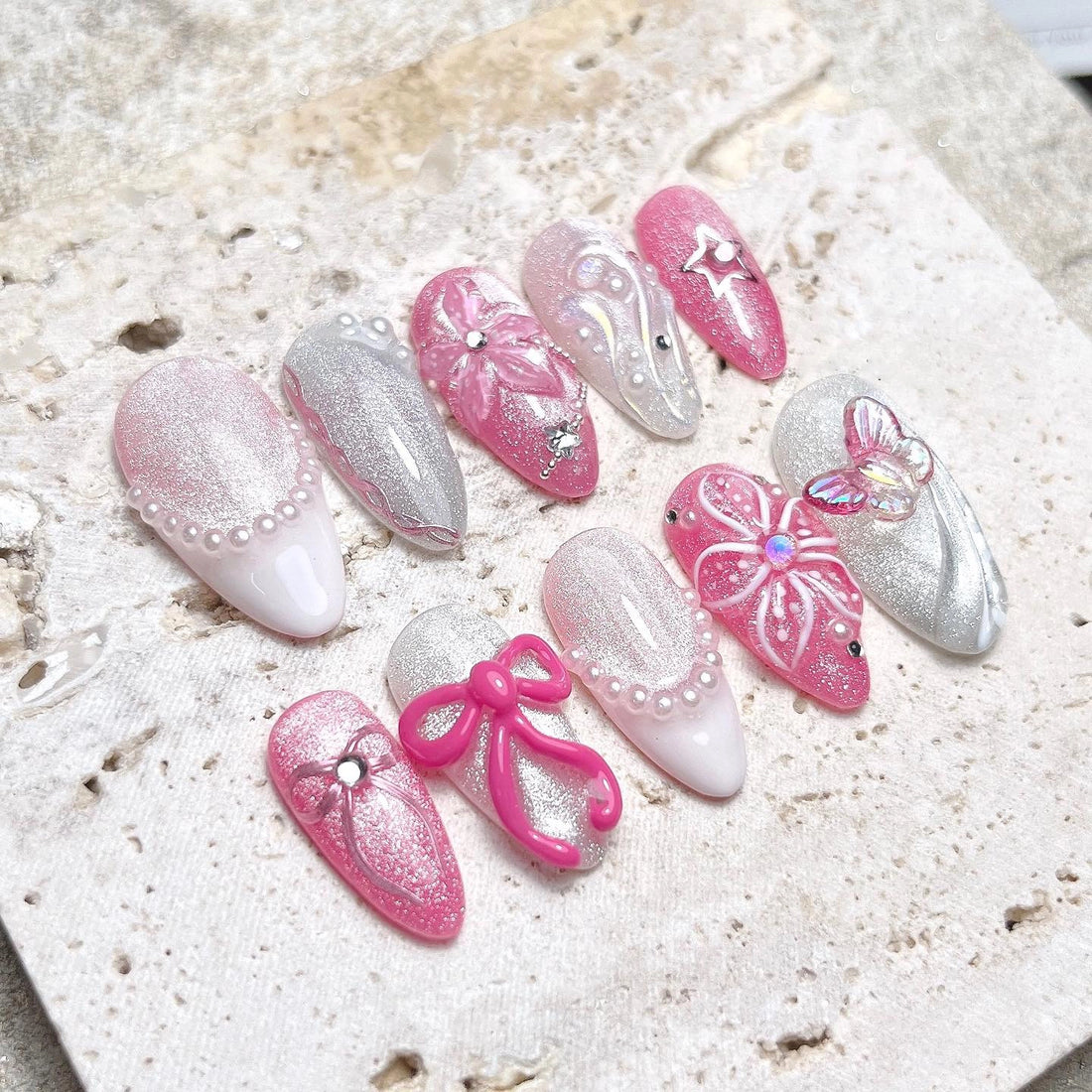 Handmade pink and silver press-on nails with 3D flowers, pearls, bows, and butterfly accents.