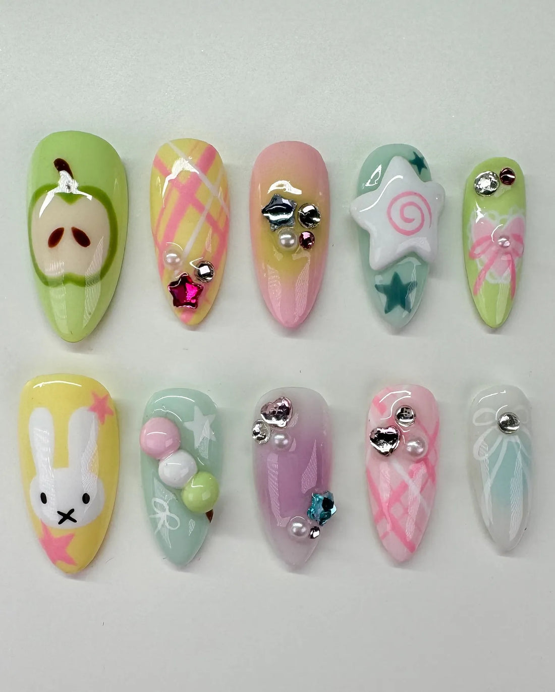 Handmade pastel press-on nails with bunny, apple, star, plaid, bows, and gem accents.
