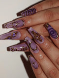 Hand with long lavender press-on nails featuring gold celestial moon, star, and sun designs.