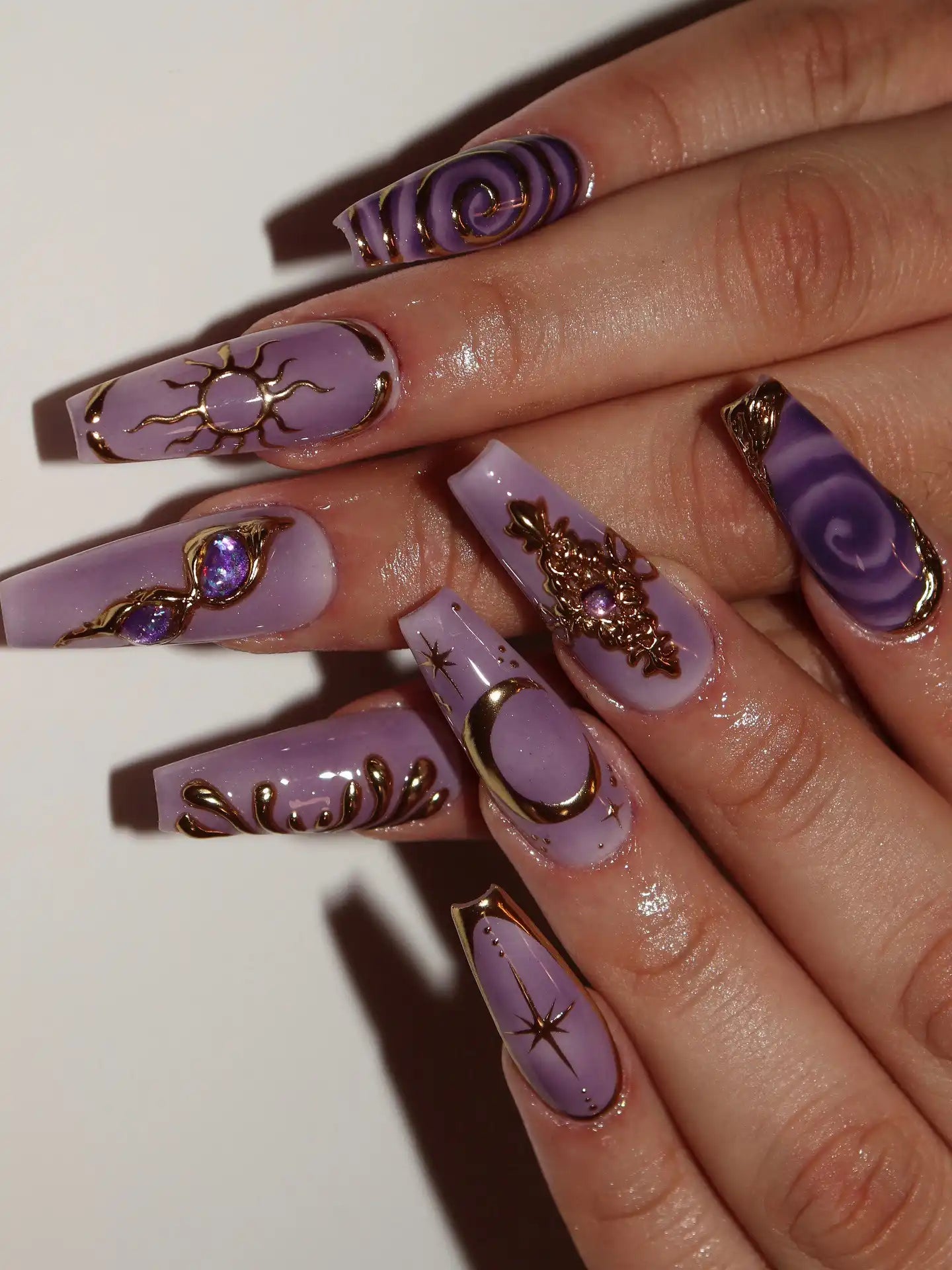 Hand with long lavender press-on nails featuring gold celestial moon, star, and sun designs.