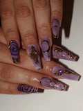 Hand with long lavender press-on nails featuring gold celestial moon, sun, and star designs
