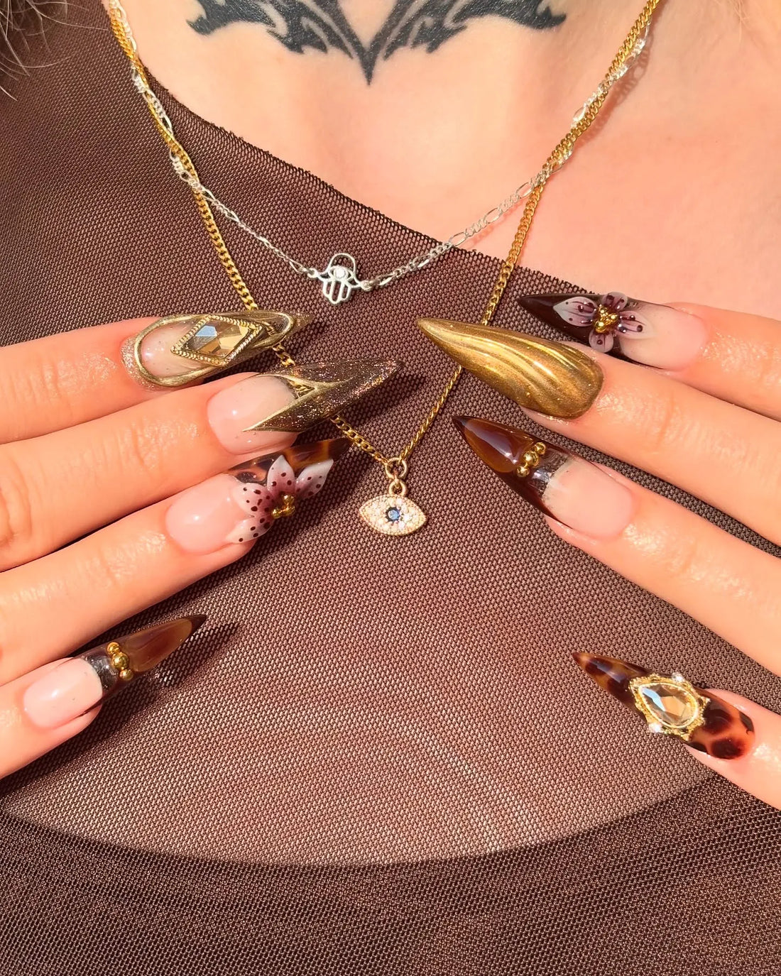 Hand with long stiletto press-on nails in tortoise shell, gold, and gem floral designs.