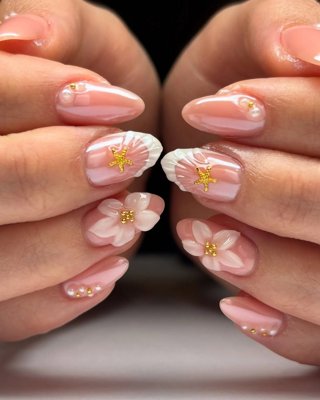 Hand with pink press-on nails featuring 3D white flowers, gold star accents, and pearl details.