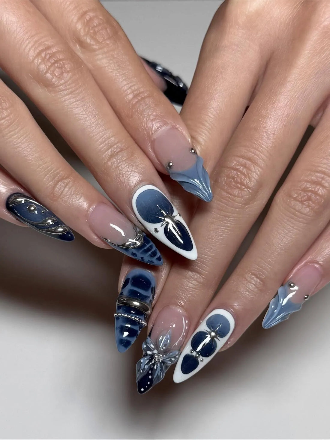 Hand with long stiletto press-on nails in midnight blue, silver chrome, 3D floral and celestial designs.