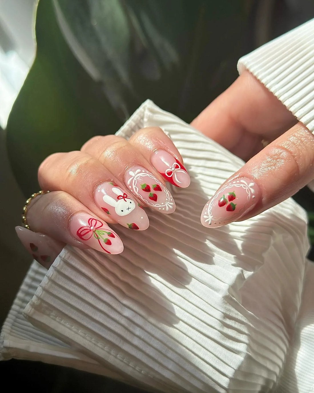 Hand with handmade press-on nails featuring strawberries, bows, lace, and a bunny design.