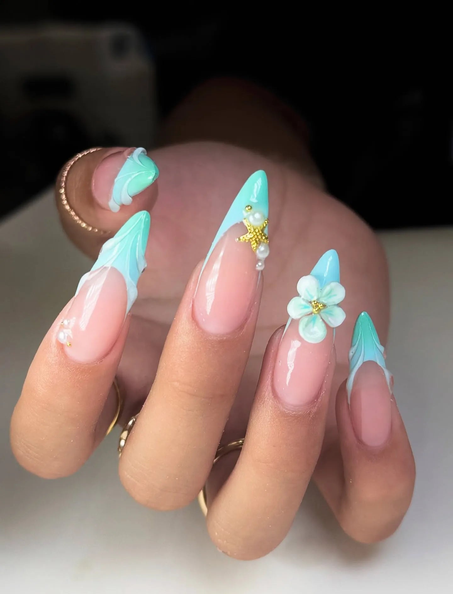 Hand with mint seafoam French tip press-on nails featuring 3D floral, starfish, and pearl accents.