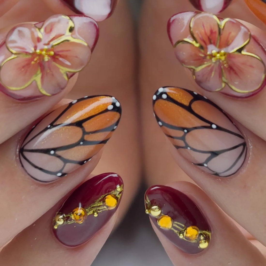 Handmade almond press-on nails with monarch butterfly wing designs, floral accents, and amber gems.
