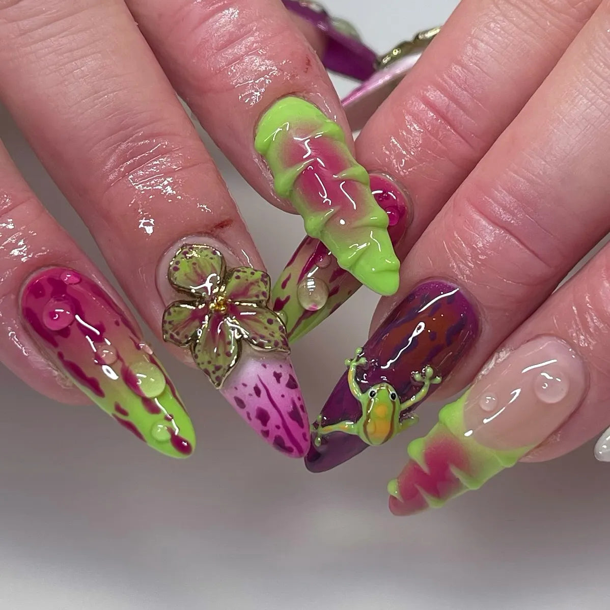 Handmade press-on nails with neon green, pink, and purple abstract drip designs, 3D flower and frog accents