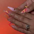 Hand with long neon orange and pink mismatched abstract press-on nails, butterfly accents