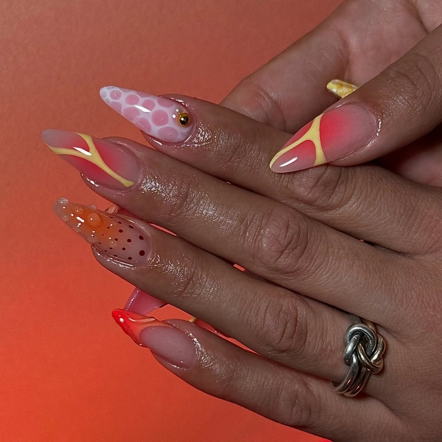 Hand with long neon orange and pink mismatched abstract press-on nails, butterfly accents