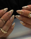 Handmade nude press-on nails with gold celestial heart and star charms, marble effect.