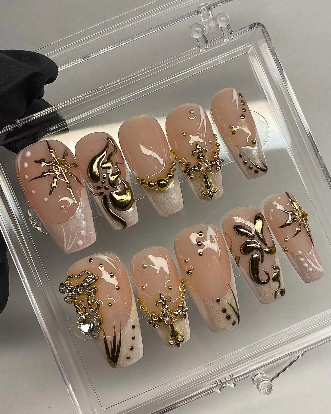 Handmade nude press-on nails with gold French tips, 3D star charms, and luxury accents in a case.