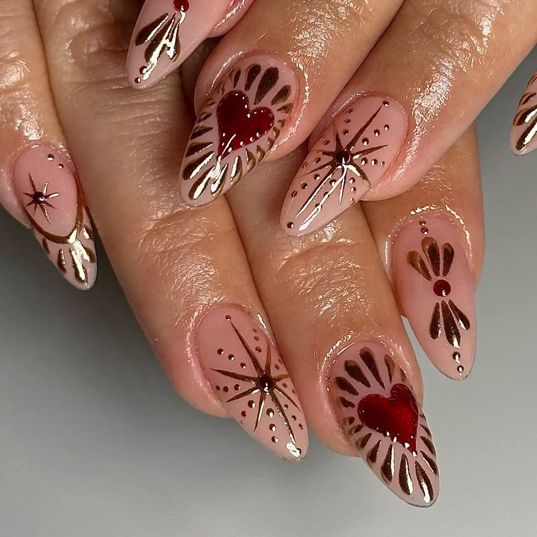 Handmade nude press-on nails with gold chrome starburst and red heart designs