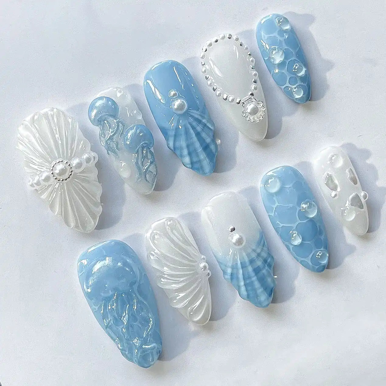 Handmade press-on nails with ocean blue jellyfish, pearls, and seashell art designs.