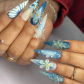 Hand with ocean blue ombre press-on nails featuring 3D floral and butterfly designs.