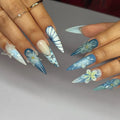 Hand with long stiletto press-on nails in blue ombré, 3D butterfly and floral nail art.
