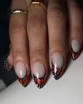Hand with handmade press-on nails featuring orange monarch butterfly wing design